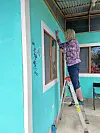 Volunteer painting a turquoise wall on a ladder.