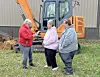 Three people talking near an excavator.