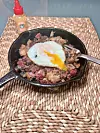 Cast iron skillet with meat and a fried egg on a placemat.