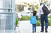 Parent and child walking on a sidewalk, holding hands.