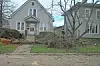 Fallen tree in front of a house with debris on the lawn.