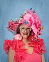 Woman with a large pink hat and ruffled pink attire smiles at the camera.