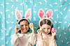 Two children with bunny ears holding colorful eggs.