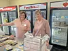 Two women volunteering at a food pantry with food items displayed.
