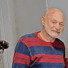 Elderly man in a striped sweater smiling indoors.
