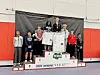 Wrestlers on podium with medals and awards.