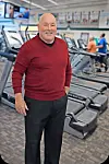 Man in a red sweater stands in a gym with exercise equipment.