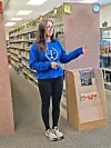 Student in a blue sweatshirt gesturing in a library.