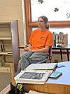 Student in orange shirt seated in classroom.