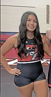 Young female wrestler in black and red uniform smiling in gym.