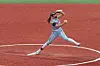 Softball player pitching on a red field.