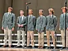 Male students singing on stage in blazers.