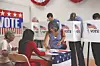 Voters at a polling station with voting booths and patriotic decor.