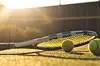 Tennis racket and balls on a court during sunset.