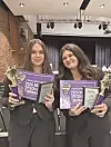 Two students holding awards and certificates in a school auditorium.