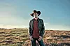 Cowboy in a field at sunset wearing a hat and jacket.