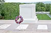 Floral wreath at a memorial site with greenery in the background.
