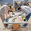 Students working on mechanical parts at a table in a workshop.