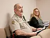 Sheriff speaking at a meeting with a woman listening.