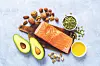 Salmon fillet, avocado halves, nuts, and seeds on a cutting board.