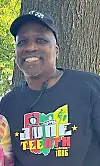 Man in a Juneteenth shirt smiling outdoors.