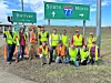 Volunteers in safety vests pose by highway signs.