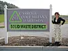Woman beside a solid waste district sign in daylight.
