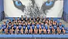 Cheerleading squad poses on bleachers in front of a wolf mural.