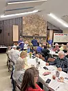 People seated at tables in a community hall.