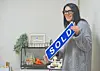 Woman holding a 'SOLD' sign in a cozy interior.