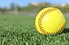 Close-up of a yellow softball on green turf.