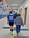 Young athlete in jersey walking with an older woman in a hallway.