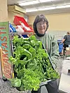 Volunteer with a tray of fresh greens in a kitchen.