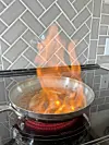 Flames rising from a frying pan on a stovetop.