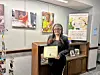 Individual holding an award certificate in a gallery setting.
