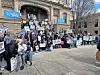 Crowd of people with signs at a rally on building steps.
