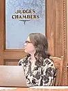 Person in judge's chambers with laptop and sign.