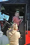 Young girl in a fire truck driver's seat with an adult nearby.