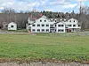 Historic white building with green shutters in a grassy area.