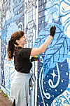 Artist painting a blue mural on a wall.