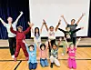 Children and adults posing with raised hands in a school gym.