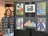 Student next to a display of colorful artworks at an exhibit.