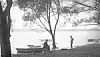 Two people by a lake with boats and trees.
