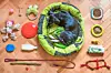 A dog curled up in a green pet bed with toys around it.