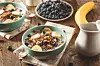 Breakfast bowls with oatmeal, banana, and blueberries on a wooden table.