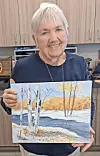 Artist smiling while holding a landscape painting of birch trees.