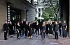 Choral group in black attire poses outside a building.