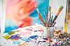 Close-up of paintbrushes in a can on a colorful artist's table.