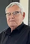 Elderly man with glasses in a black shirt indoors.