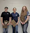 Three students with clipboards in a competition setting.